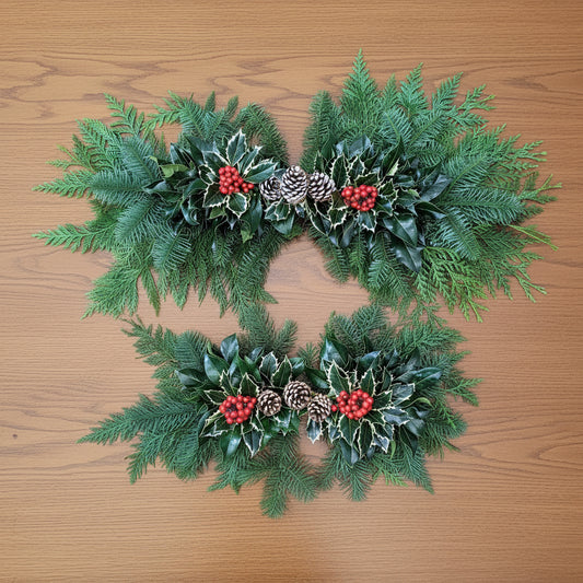 Two festive centerpiece with greenery, berries, and pinecones on a wooden table.