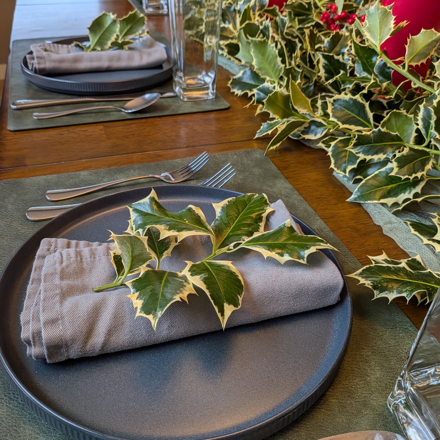 Dining table setting with holly leaves on a plate and green placemats.