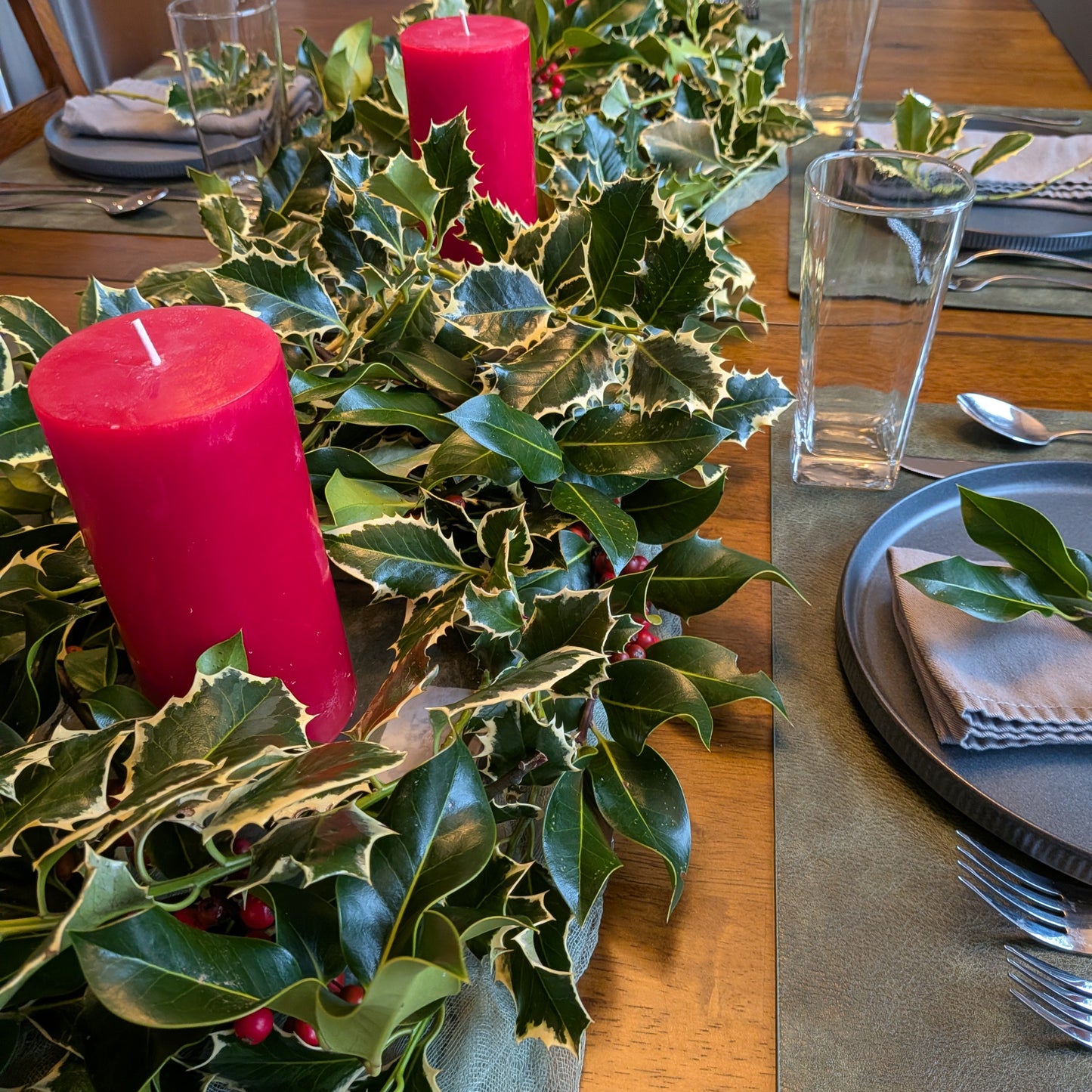 Decorative table setting with holly leaves, red candles, and place settings.